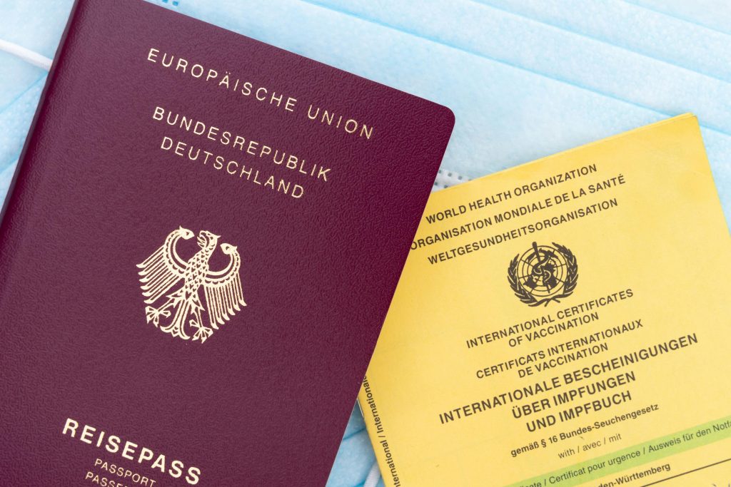 pexels-photo-6815940-6815940 Close-up of a German passport, vaccination card, and face mask, symbolizing travel and health documentation.